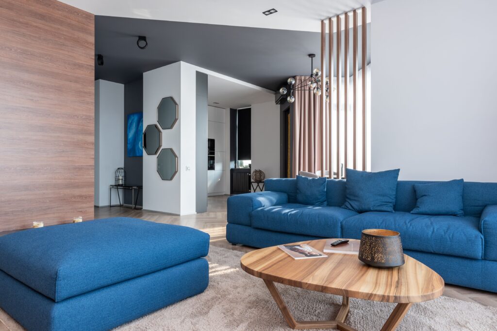 Interior of contemporary flat with blue couch and pouf placed near table in living room near kitchen zone with decorations on wall